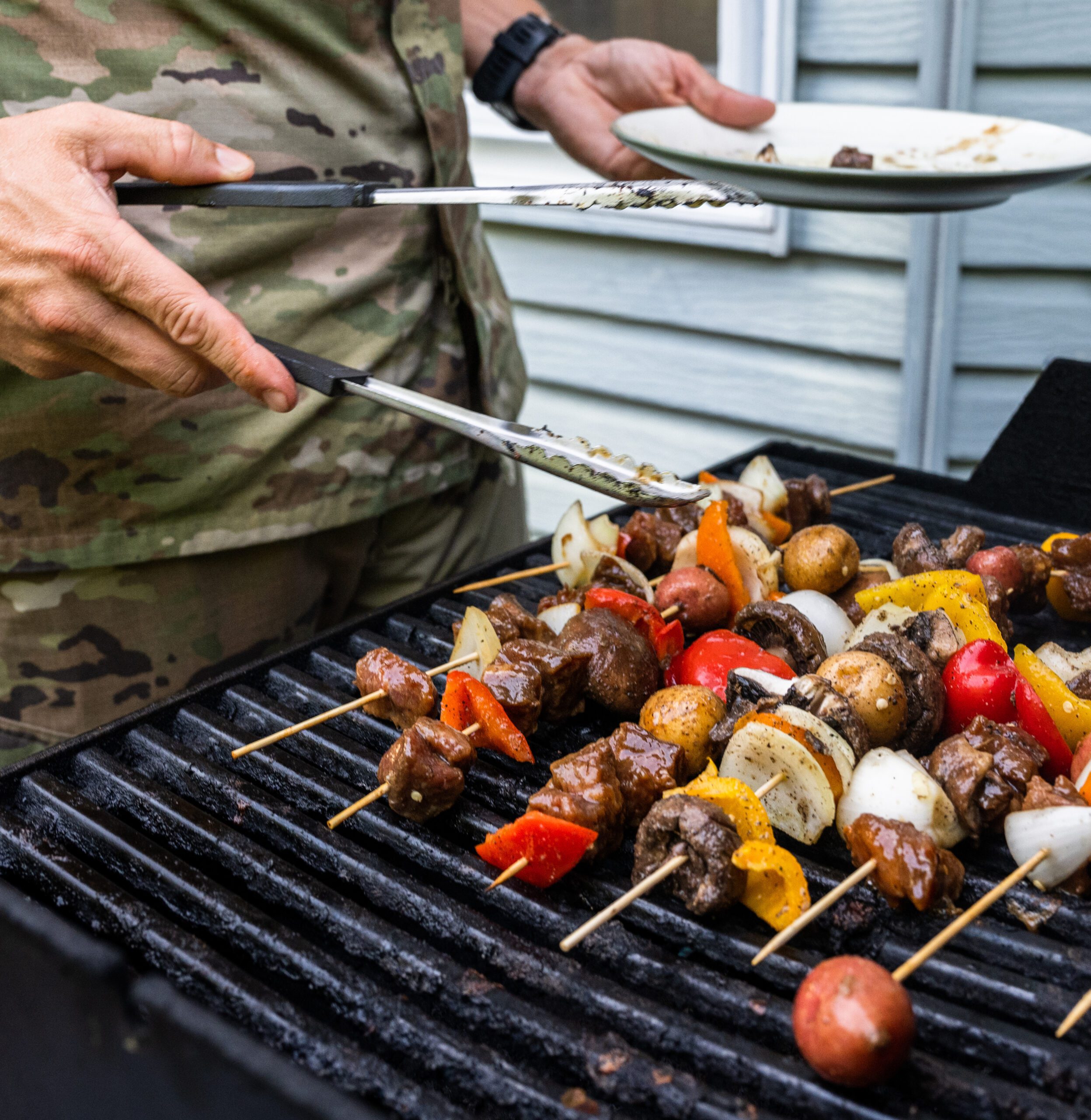 Military servicemember grills kebabs on base.